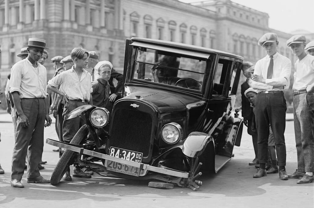 group of boys standing besides a broken car