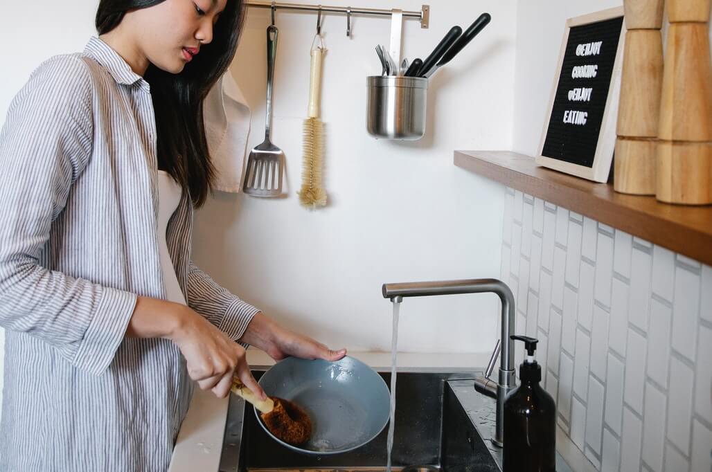 woman washing piled up dishes in the sink