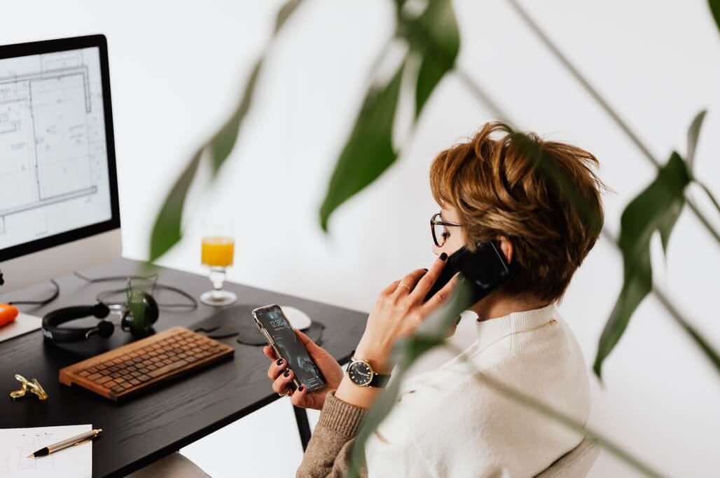 woman talking on her phone, scrolling a phone and working on a computer at the same time