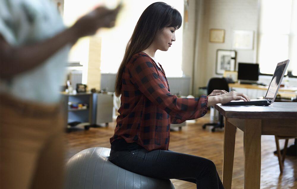 woman sitting on a medicine ball while working from home